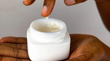 A hand scooping Xoxoderma cream from an open jar.